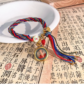Detailed close-up of handmade woven bracelet with golden charms and miniature scroll pendant