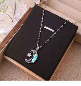 Gros plan du pendentif lune et étoile en nacre d'abalone sur un support noir