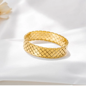 Dettaglio di un ampio bracciale in acciaio al titanio dorato con motivo a griglia a trifoglio
