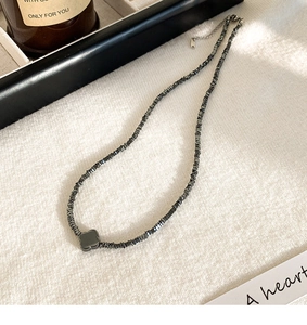 Detailweergave van de zwarte klaverhanger en donkergrijze steenketting op linnen ondergrond