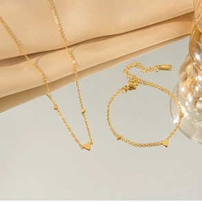 Dettaglio del set collana e bracciale con cuori dorati su seta beige con riflesso