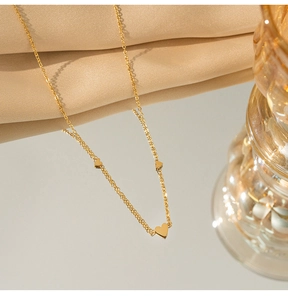 Dettaglio della collana a cuore dorata a strati su seta champagne con riflesso specchio