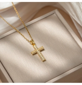 Close-up of a gold-plated cross pendant with sparkling crystals on a fine cable chain