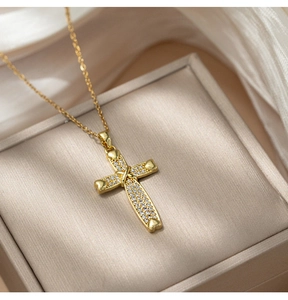 Close-up of gold cross pendant with cubic zirconia and heart details in jewelry box