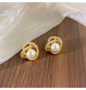 Détail de boucles d'oreilles camélia dorées avec perles et zircons sur bois