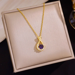 Detailopname van gouden ketting met druppelvormige paarse zirkoon hanger en hartje