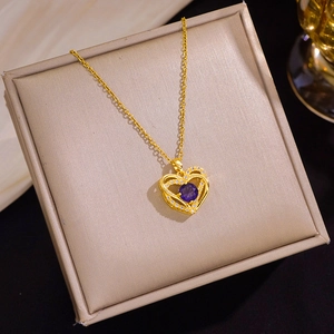 Detail van een gouden hartvormige hanger met paarse zirkoon in een geschenkdoos
