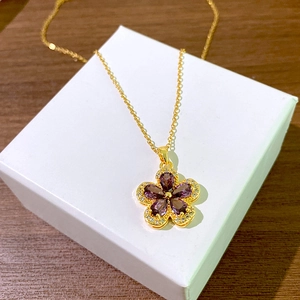 Elegante gouden titanium ketting met paarse zirkoon bloemhanger op een wit juwelendoosje
