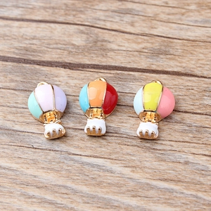 Détail de pendentifs montgolfière en émail pour bijoux DIY sur fond de bois clair naturel