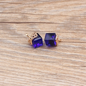 Macro shot of dark blue crystal cube earrings with intricate gold hollow patterns