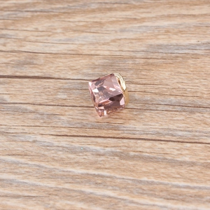 Detailed view of a pink cube crystal pendant with a gold metal base on wood surface