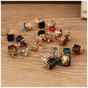 Colorful cube glass crystal pendants with gold caps on a natural wooden background
