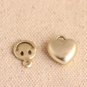 Golden alloy charms featuring a hollow smiley face and a puffy heart on beige fabric