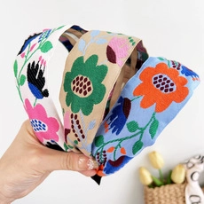 Close-up of three handmade floral embroidered headbands in white, beige and blue fabric