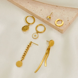 Close-up of gold stainless steel earrings with butterfly and star charms on stone surface