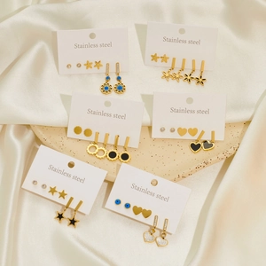 Golden stainless steel earring set with heart, star, and eye motifs on silk fabric