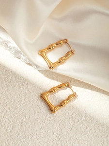 Details von goldenen Titan-Ohrringen in Bambus-Optik auf Seide und Stein