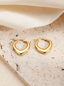 Poliertes Gold-Herz-Ohrringe auf beige Steinstruktur mit weichem Seidenstoff