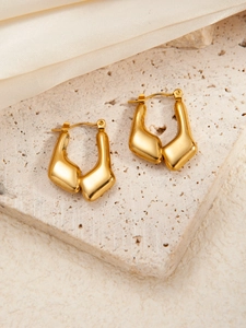 Polierte goldene geometrische Ohrringe auf Steinfläche mit eleganter Seide im Detail