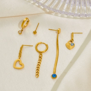 Close-up of golden hollow heart and evil eye charms on stainless steel earrings