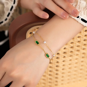 Detail of double-layer gold chain bracelet with emerald green stones and white pearls