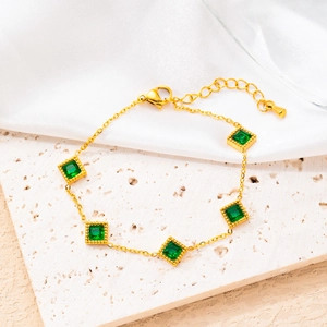 Detail of gold chain bracelet with five square green gemstones on white marble
