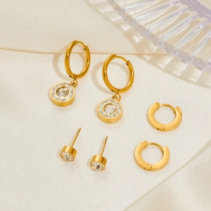 Three pairs of golden stainless steel earrings with crystals on a silk fabric background