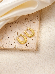 Detail goldener U-förmiger Creolen mit Wabenstruktur auf Stein- und Satinhintergrund