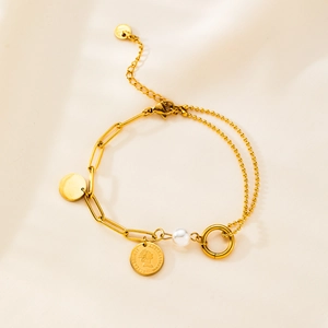 Detail of gold layered bracelet with coin pendant and white pearl on silk background