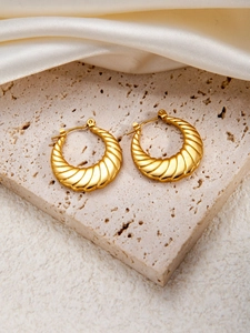 Detailansicht goldener Croissant-Ohrringe mit Spiralstruktur auf Travertin-Oberfläche