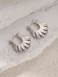 Detail van zilveren schelpvormige titanium stalen oorringen op een witte stenen ondergrond