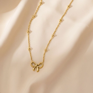 Elegante goldene Schleifen-Halskette mit Perlenkette auf beige Seidenhintergrund