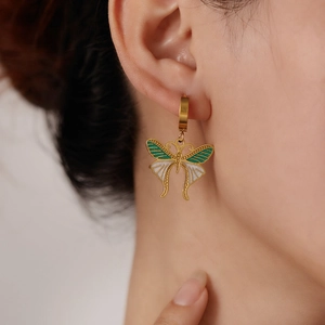 Detail of gold butterfly drop earrings with green and white enamel on a model ear