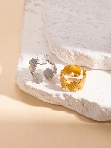 Detailed close-up of gold and silver leaf-shaped textured rings on white stone