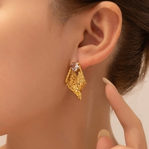 Detalle de pendientes dorados geométricos con metal texturizado y circonita cuadrada