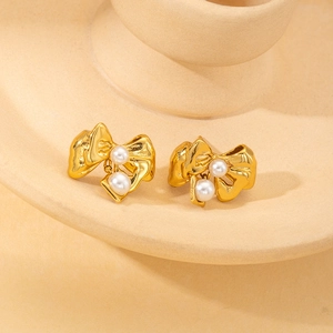 Detail of gold bow earrings featuring textured metal finish and central white pearl accent