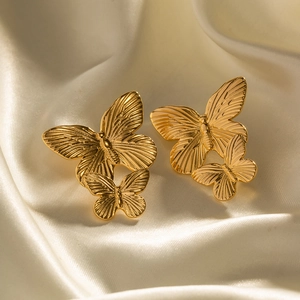 Detail view of gold butterfly stud earrings on soft silk fabric texture background