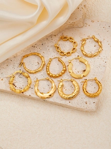 Set of nine golden hoop earrings with diverse textures on beige stone and silk cloth