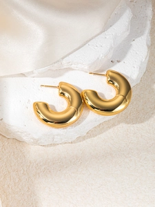 Detailed close-up of chunky gold C-shaped earrings on stone with silk background