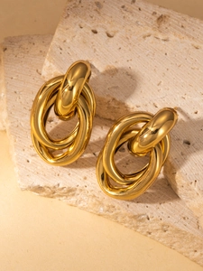Primer plano de aretes de titanio dorado con triple eslabón sobre piedra texturizada