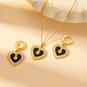 Elegant gold heart jewelry set with black enamel and diamonds on a white ceramic plate