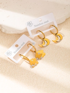 Détail de boucles d'oreilles créoles bicolores en acier avec breloques lune et papillon