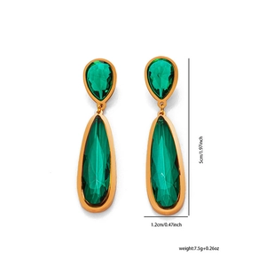 Detalle de pendientes largos dorados con piedras verdes en forma de pera facetada