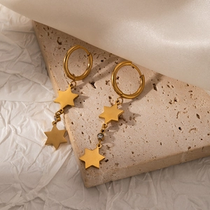 Detailed macro of golden star drop earrings featuring round cubic zirconia on beige stone