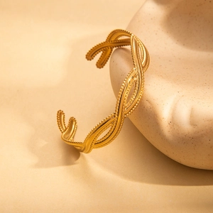 Nahaufnahme des goldenen unregelmäßigen Armreifs mit Kordeldesign auf beigem Grund