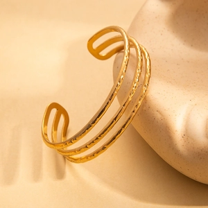 Detail eines mehrlagigen goldenen Armreifs mit Hammerschlag-Struktur und glänzendem Finish