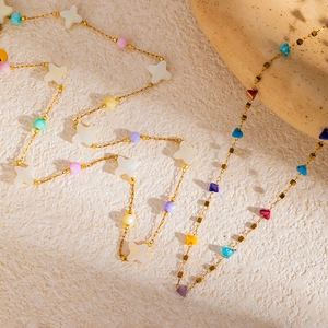 Colorful beaded necklace with golden chain and white shell star charms on a textured background