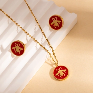 Dettaglio di orecchini e collana con api dorate e inserti in smalto rosso vivace