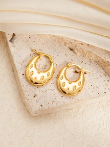 Detailed close-up of golden titanium steel earrings with textured oval groove patterns