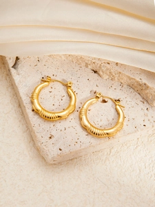 Elegant gold hoop earrings with embossed texture on silk and stone background